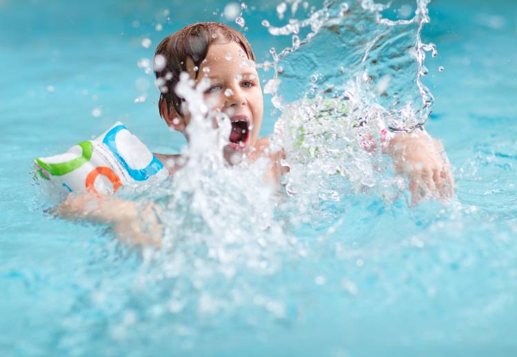 Young Boy Splashing Water In Swimming Pool